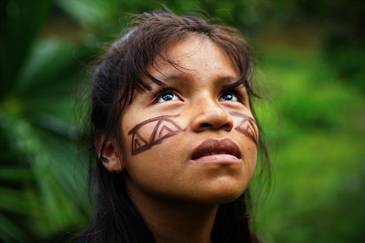 Young girl with tribal markings stares into the amazon rainforest canopy
