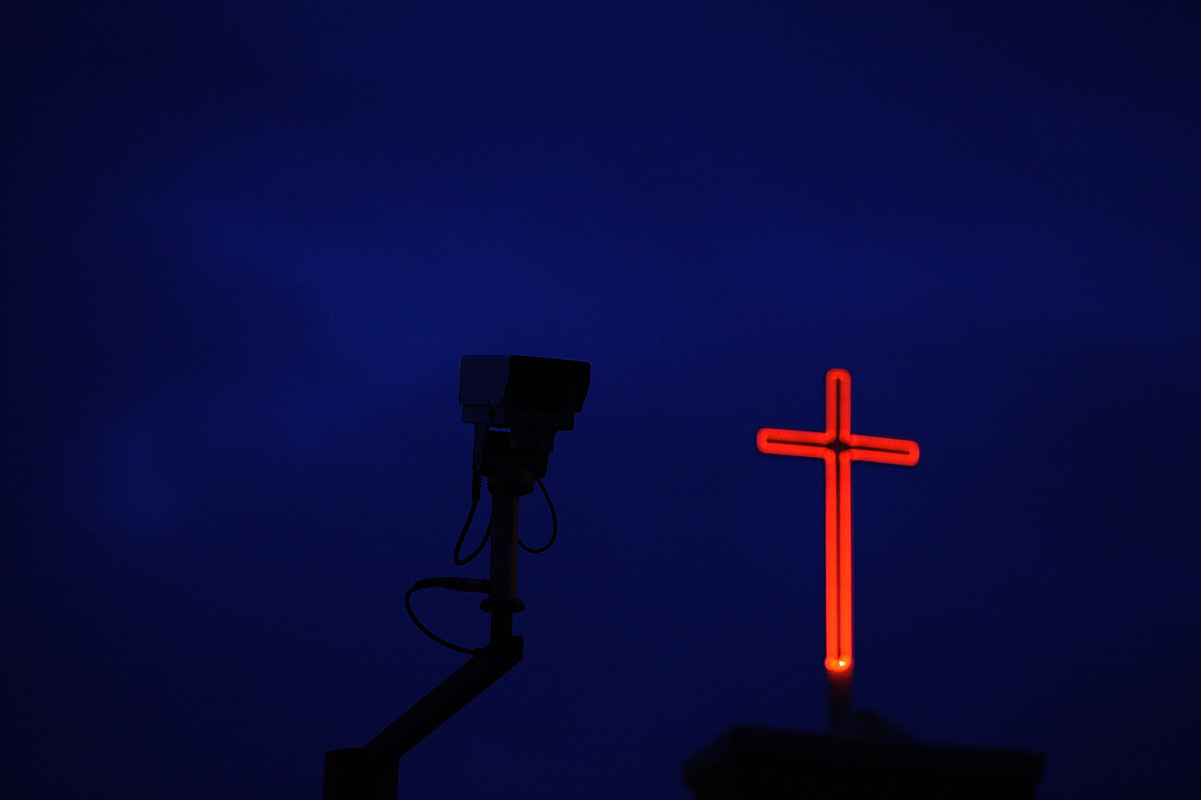 Ominous security CCTV camera watches with Christian red cross in background